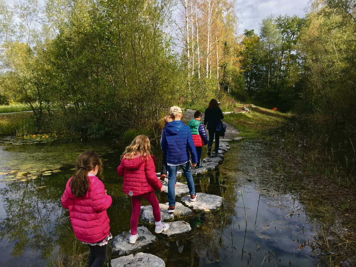 Man sieht Kinder ein Gewässer auf Steinen überqueren.